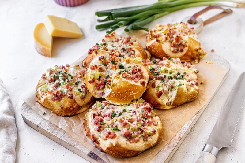 Laugenbrötchen mit Käse und Speck überbacken auf Holzbrett