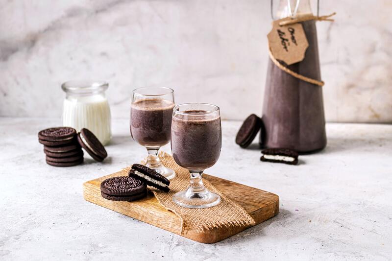 Zwei Schnapsgläschen mit Oreo-Likör auf Holzbrett mit angelegten Oreo-Keksen