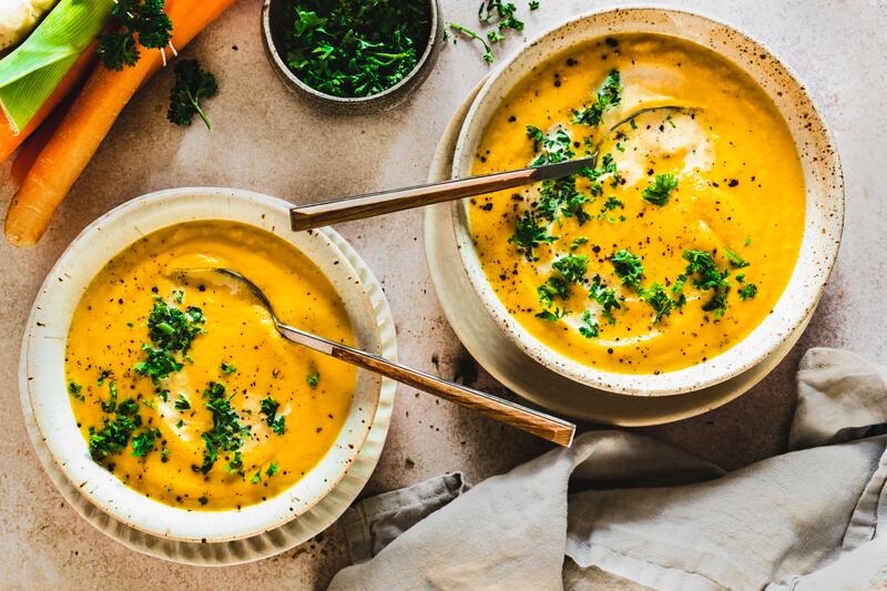 Gelbe Low-Carb-Gemüsesuppe in zwei tiefen Tellern mit Kräutern
