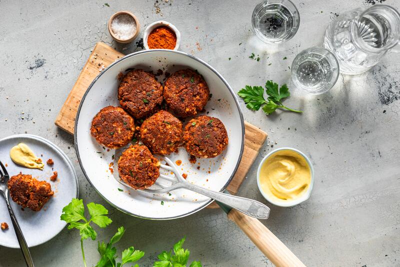 Tofu-Hackbällchen in weißer Pfanne auf Holzbrett mit angestellten Gewürzen