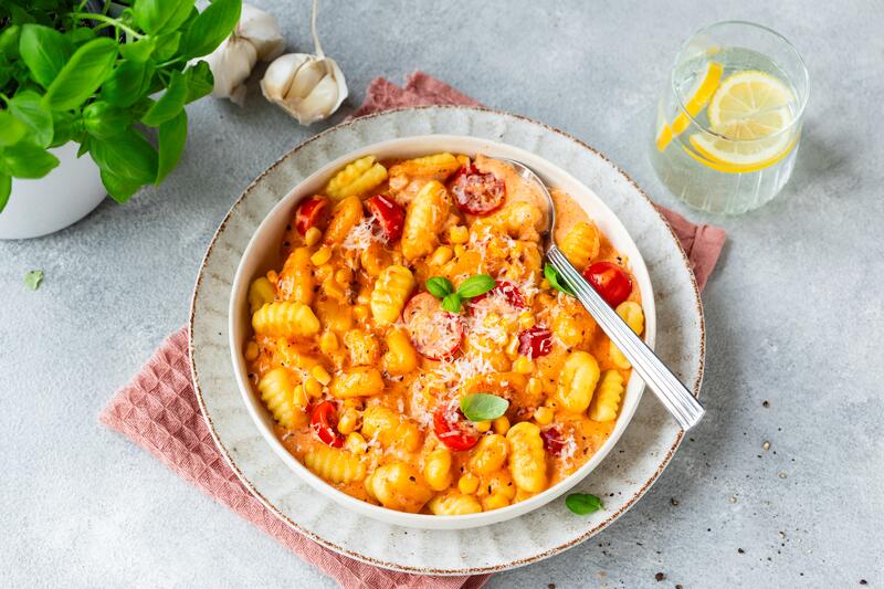 Cremige Gnocchi mit Tomaten und Mais in tiefem Teller mit Löffel