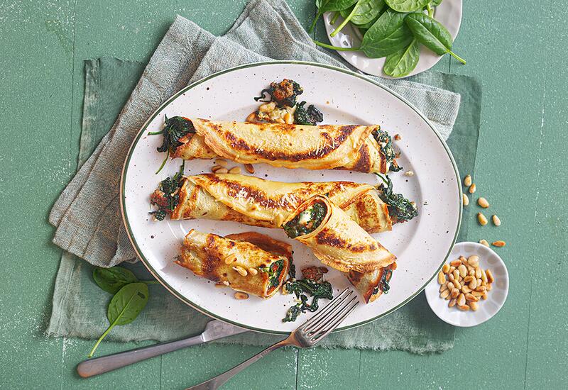 Pfannkuchenröllchen mit Spinat und Salsiccia auf weißem Teller