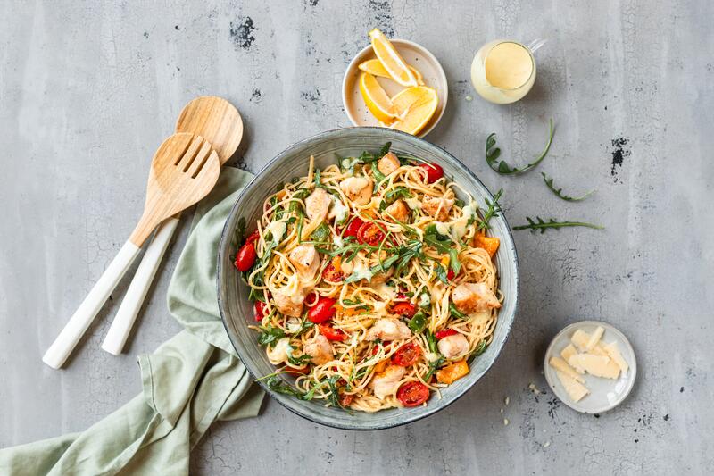 Ein Teller mit Nudelsalat von oben, darin Tomaten, Kräuter, Spaghetti