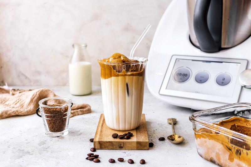 Ein Glas mit Dalgona-Eiskaffee, im Hintergrund der Thermomix®