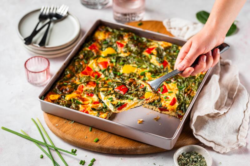 Blech mit Frittata mit Gemüse, eine Hand hebt ein Stück heraus