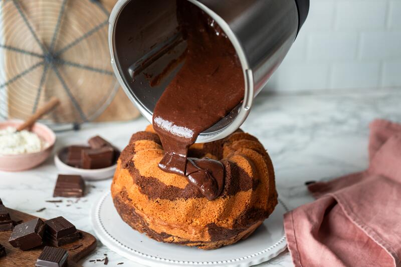 Mixtopf mit Schokoglasur wird über einen Gugelhupf-Kuchen gegossen