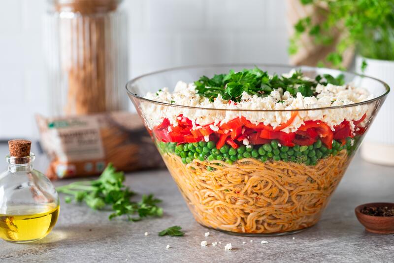 Große Glasschüssel mit Spaghetti und Gemüse und Feta Schichten