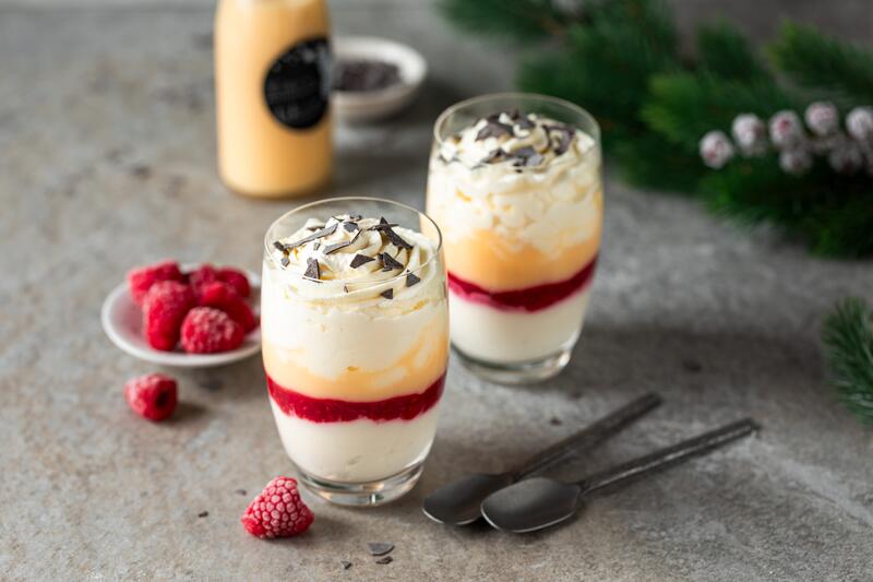 Zwei Gläser mit Eierlikör Dessert gefüllt, daneben Schüsselchen mit Himbeeren