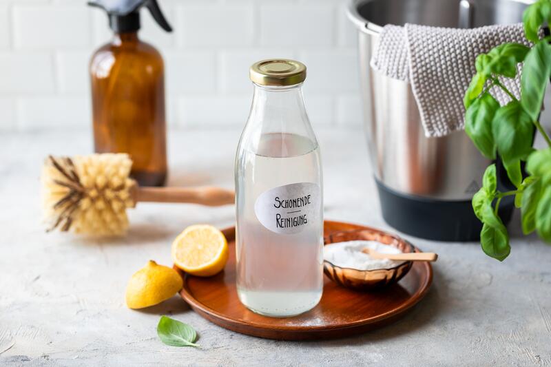 Glasflasche mit selbst gemachtem Reinigungsmittel, daneben eine halbierte Zitrone und Backpulver