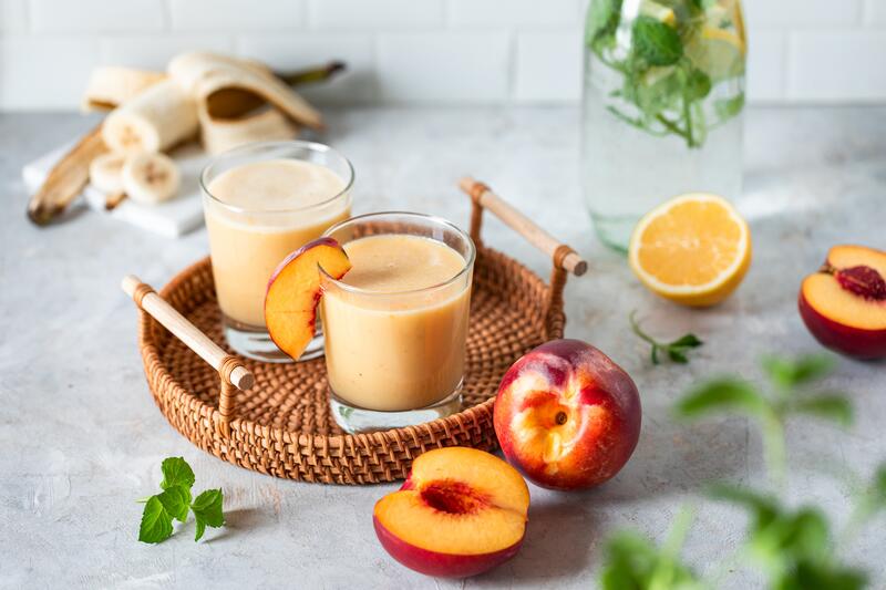 geflochtenes Tablett mit zwei Gläsern, gefüllt mit hell orangenem Saft, dazu Nektarinen als Deko