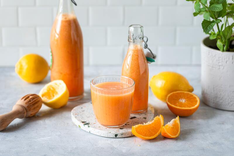 Orangener Saft in Flaschen und ein Glas umgefüllt, daneben Zitronen und Orangen auffgeschnitten