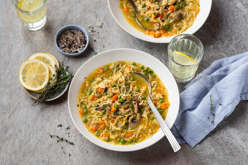 Zwei Schüsseln mit Anti-Erkältungssuppe mit Gemüse, danben Gläser mit Zitronenwasser