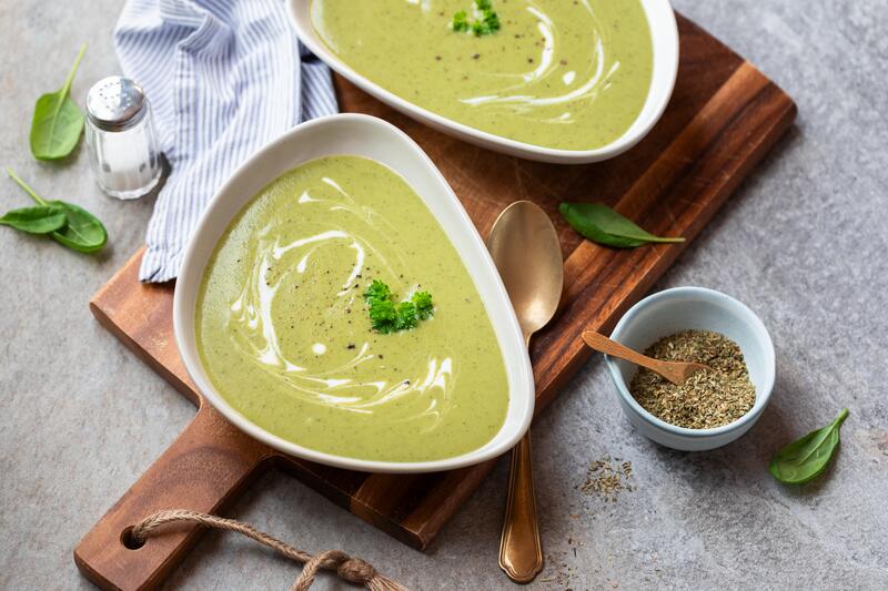 Holzbrett mit zwei Schüssel drauf, darin grüne Suppe mit weißer Creme getoppt