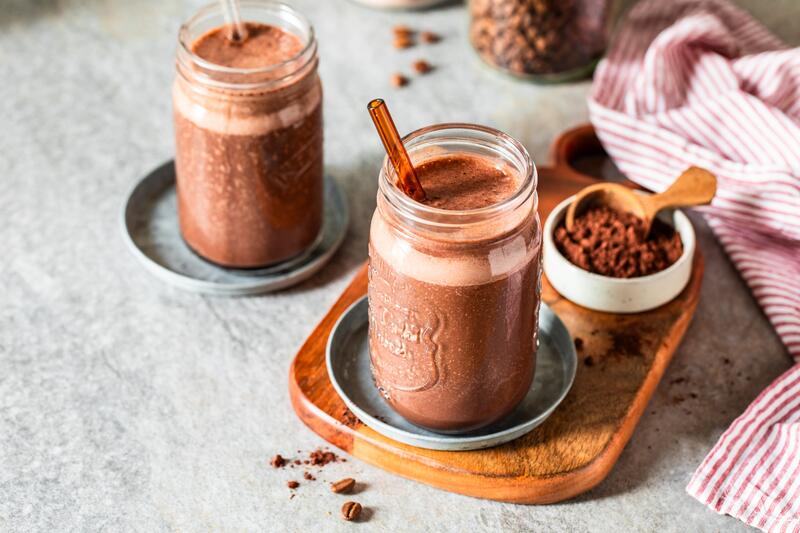 Zwei Gläser mit braunem Shake, daneben eine kleine Schüssel mit braunem Pulver