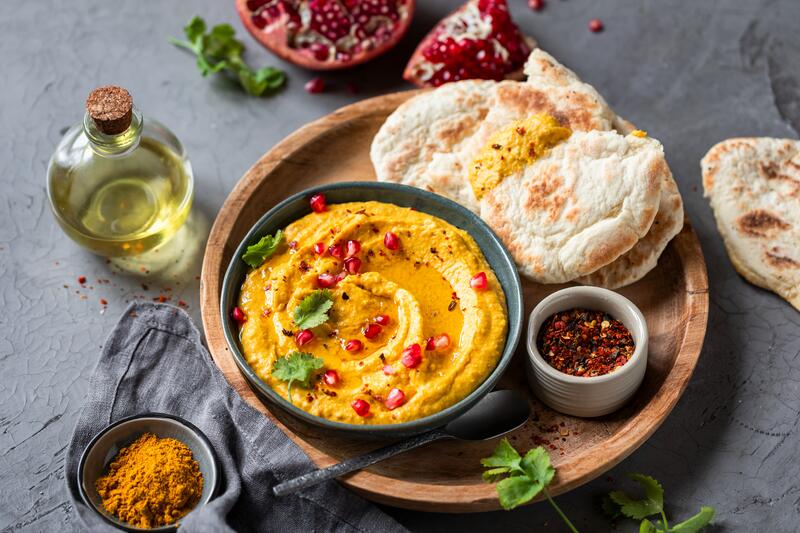 Schüssel mit gelbem Dip, daneben Fladenbrot und Mango und Granatapfel