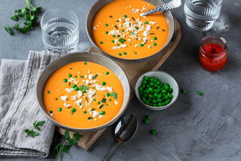 2 Schüsseln mit orangener Suppe, darauf Feta zerbröselt, Erbsen und Petersilie