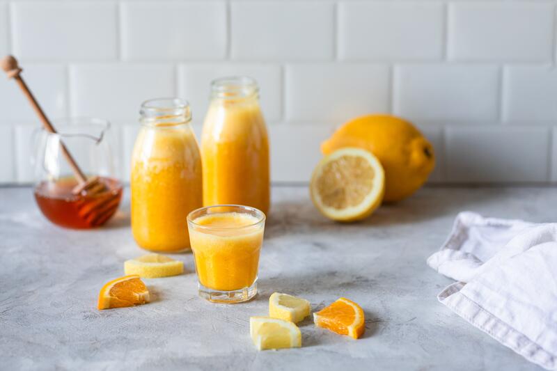 Zwei Flaschen und ein Glas gefüllt mit gelbem Winter-Vitaminchen-Saft