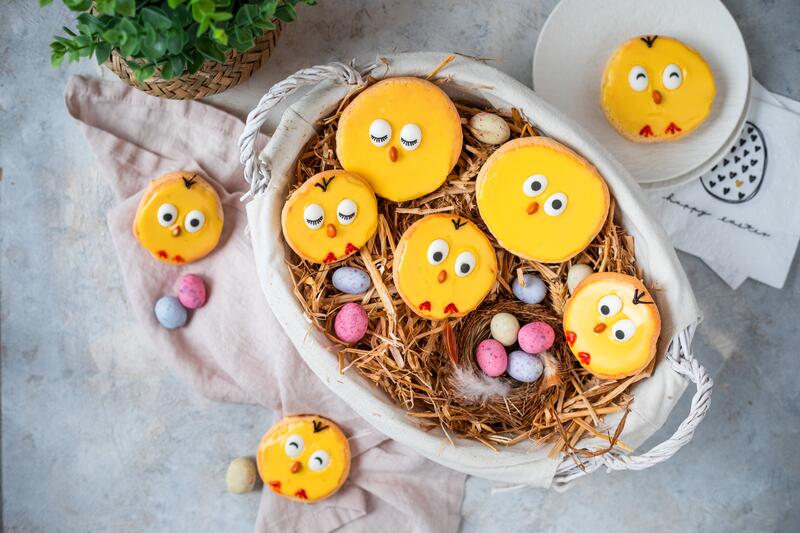 Auflaufform mit Stroh und bunten Mini-Eiern, darin liegen die als Küken verziehrten Amerikaner