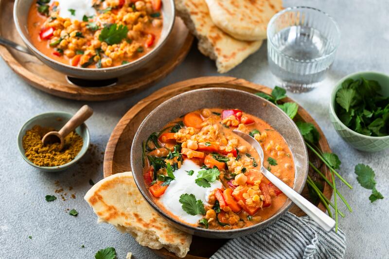 Linsencurry mit Kichererbsen in einer Schüssel mit Gemüse und Joghurt darauf