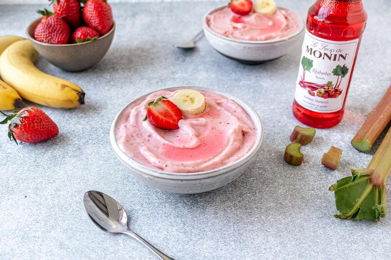 Zwei Schüsseln mit rosa Creme und Erdbeeren und Bananen verziert