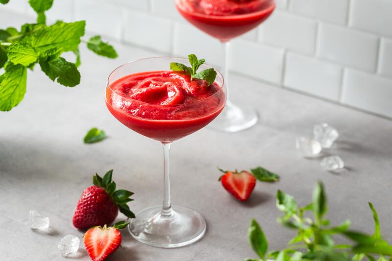 Martini Gläser mit gefrorenem rotem Cocktail und Erdbeeren als Deko, daneben eine Flasche Erdbeersirup von Monin