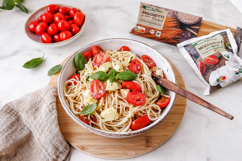 Dinkel-Spaghettisalat Tomate-Mozzarella auf einem Teller von oben fotografiert, daneben Tomaten