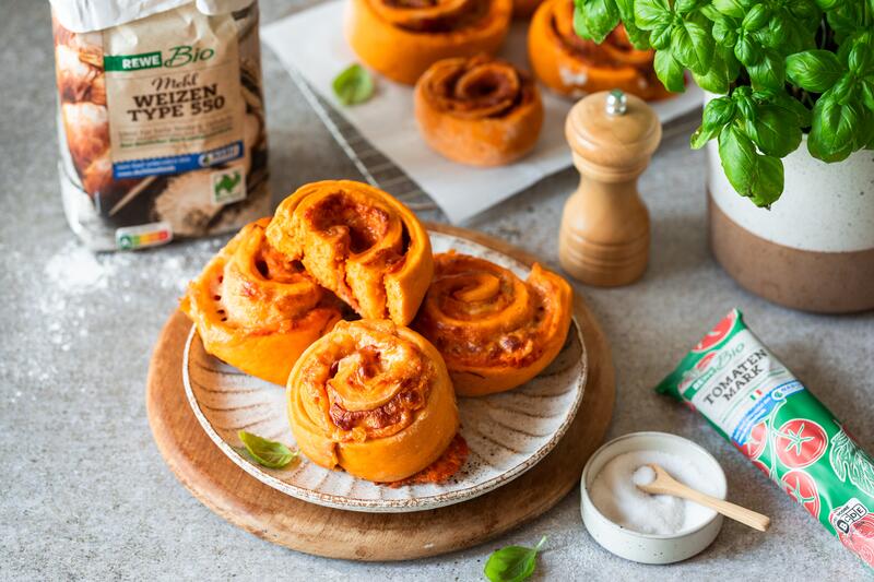Teller mit 4 Pizzaschnecken, daneben eine Packung Mehl und Tomatenmark