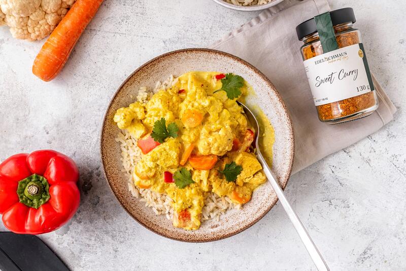 Ein Teller mit Reis-Hähnchen und Gemüse von oben fotografiert, daneben ein Paprika, Karotte und ein Sweet Curry Gewürz
