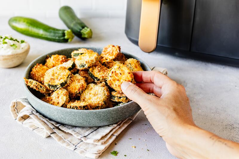 Tiefer Teller mit knusprigen Zucchini-Bites und Airfryer im Hintergrund