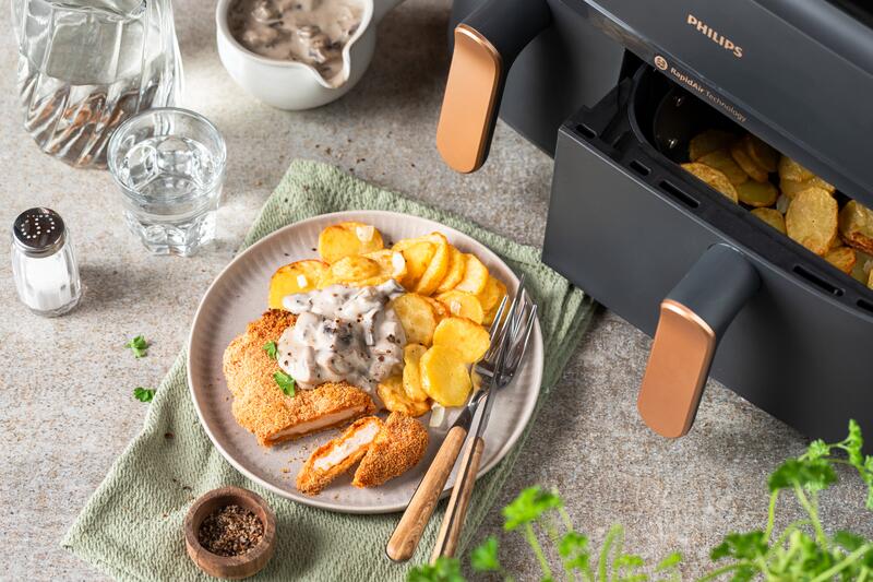 Teller mit Schnitzel und Bratkartoffel, vor einem Airfryer