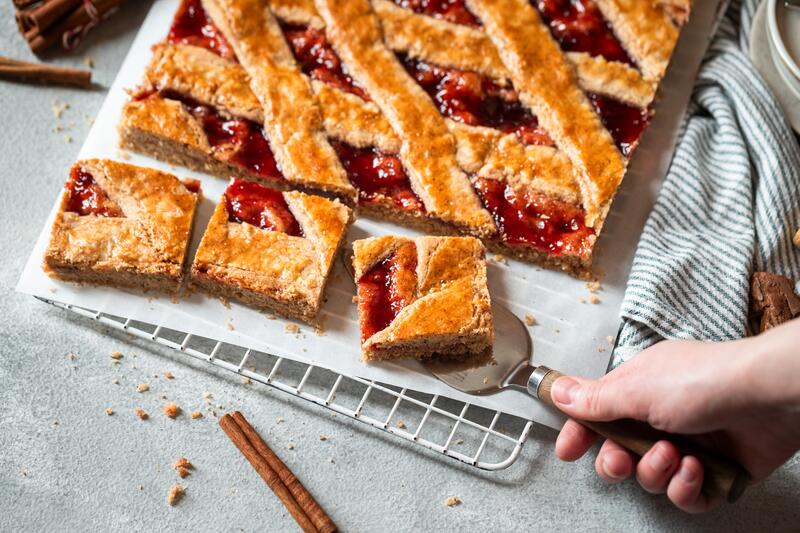 Angeschnittene Linzertore mit Marmelade auf einem Blech angeschnitten, eine Hand nimmt ein Stück