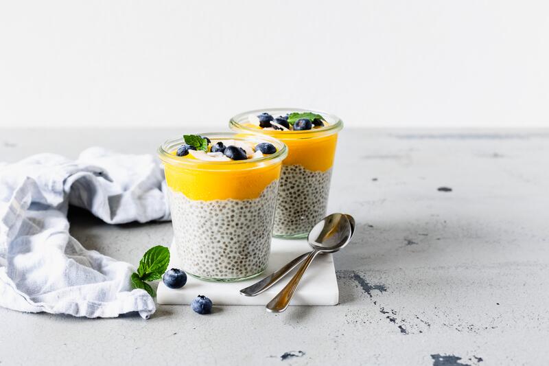 Zwei Gläser mit Chiapudding und Mangopüree, mit Minze und Blaubeeren garniert