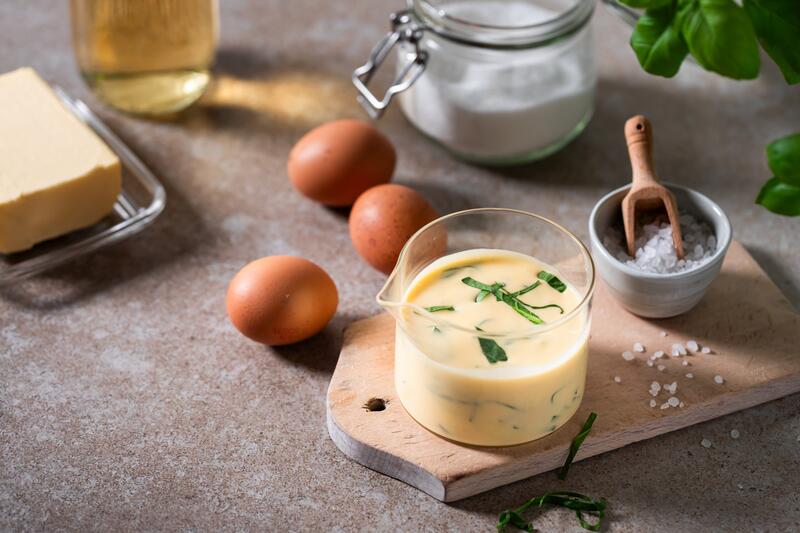 Glasschale mit Hollandaise und Bärlauch getoppt, daneben liegen Eier