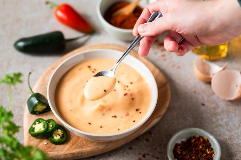 Hand rührt orange Mayo in einer Schüssel um, daneben Chilis