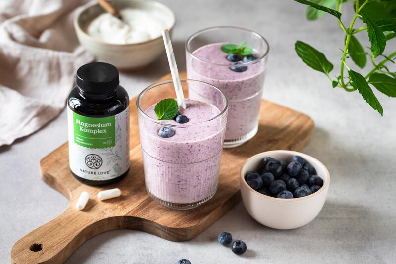 Zwei Gläser mit Blaubeer-Smoothie, danebenglas mit Nahrungsergänzungsmittel