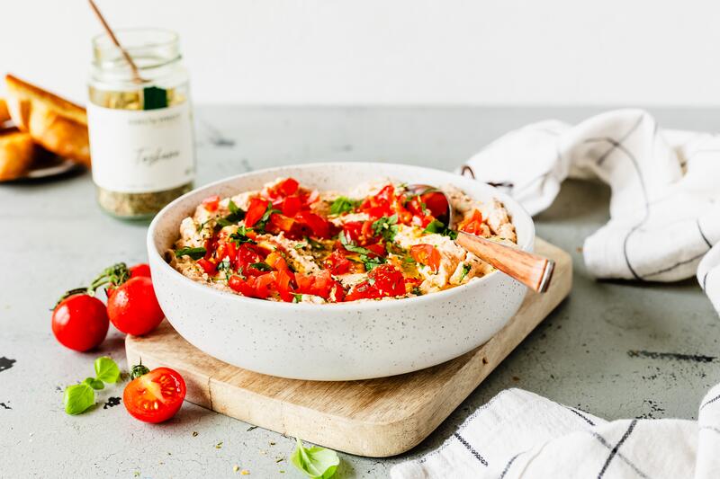 Schüssel mit cremigem Dip, Tomatenstücken und Kräutern, im Hintergrund Edelschmaus Gewürzmischung
