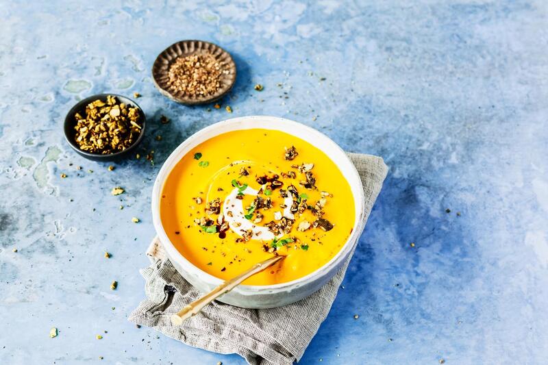 Kürbissuppe in einer hellen Schale auf hellblauem Untergrund