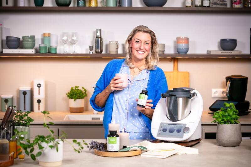 Blonde Frau mit einem Thermomix® und einem Glas mit Magnesium-Tabletten