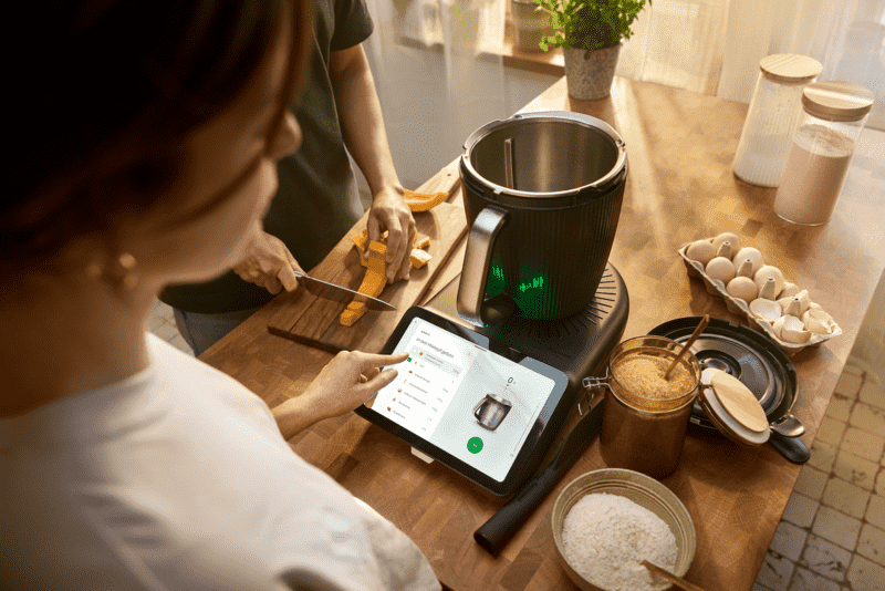 Eine Frau steht vor dem Thermomix® TM7 und bedient das Display