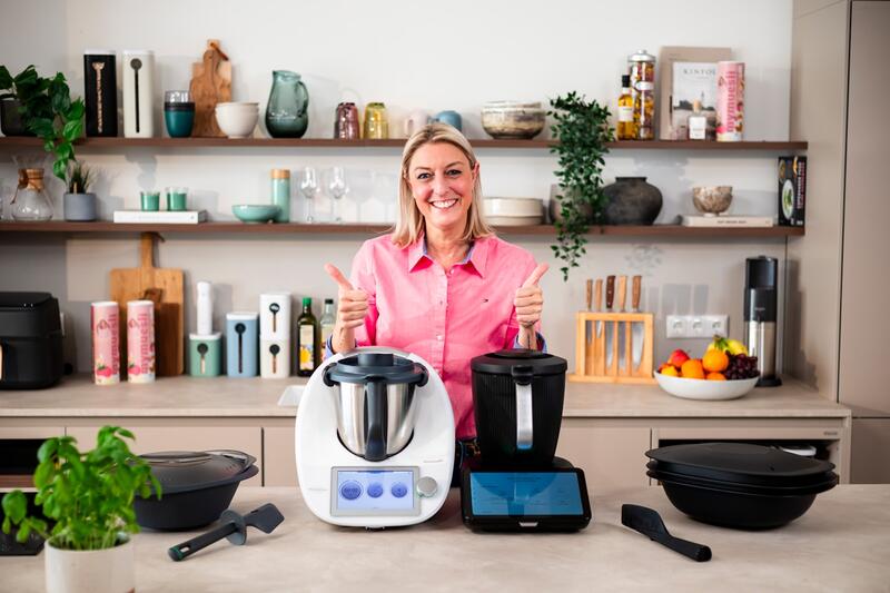 Eine blonde Frau steht hinter Thermomix® TM6 und TM7 und hält beide Daumen hoch