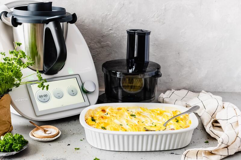 Der Thermomix® TM6, daneben der Wunder Slicer Aufsatz und eine Auflaufform mit Kartoffelgratin