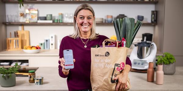 Dési vom ZauberTopf Club mit einer Einkaufstüte voller Lebensmittel von REWE