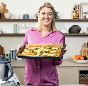 Blonde Frau mit einem Blech Pizza