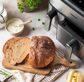 Mischbrot angeschnitten auf Holzbrett, danaben der Airfryer von Philips