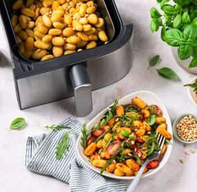 Zwei Schalen mit Gnocchi, Ruccola, Tomaten, von oben fotografiert, daneben der Airfryer
