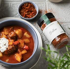 Eine Schale mit Gulasch, daneben ein Glas mit Balkan-Gewürz