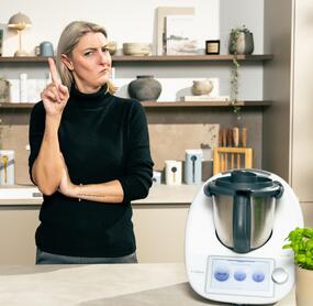 Blonde Frau in einer Küche neben dem Thermomix®, kritisches Gesicht