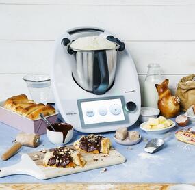 Der Thermomix® mit Hefeteig im Mixtopf und umgeben von verschiedenem Gebäck