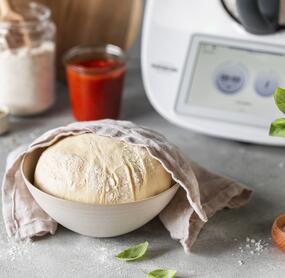 Halb abgedeckter Pizzateig in einer Schüssel.