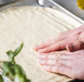 Hände streichen Pizzateig glatt